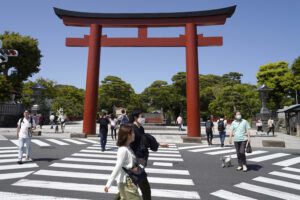 In this May 17, 2020, photo, people walk past the torii, a gateway at the entrance to Tsurugaoka Hachimangu Shinto shrine, in Kamakura, Kanagawa prefecture, near Tokyo. While Kanagawa is still under a coronavirus state of emergency, the pandemic is pitting those willing to follow requests for self-restraint against a sizable minority resisting the calls to stay home. (AP Photo/Shuji Kajiyama)