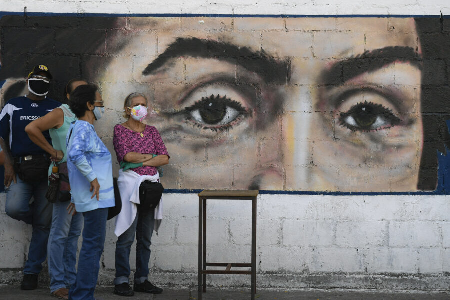 People wearing masks to curb the spread of COVID-19 wait to vote in front of a mural of the eyes of Venezuelan independence hero Simon Bolivar during a voting rehearsal at a public school in the Catia neighborhood of Caracas, Venezuela, Sunday, Oct. 25, 2020. Venezuela’s electoral authority is testing the voting process in preparation for the Dec. 6 parliamentary elections. (AP Photo/Matias Delacroix)