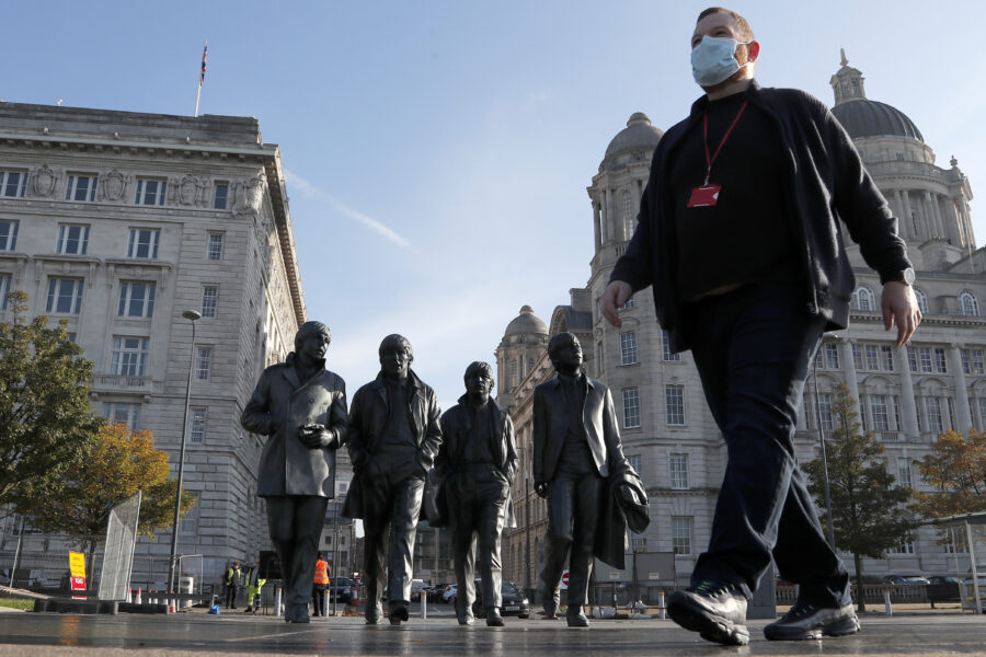 John Ambrose, a guide with the Beatles-themed Fab4 Taxi Tours, wears a face mask as he walks past a statue of the Beatles in Liverpool, England, Wednesday, Oct. 14, 2020. The English port city that gave the world the Beatles weathered decades of industrial decline before becoming a celebrated symbol of urban renewal. Now, the coronavirus is putting Liverpool’s hard-won revival in jeopardy, and raising tensions between the north of England and the wealthier south. (AP Photo/Frank Augstein)