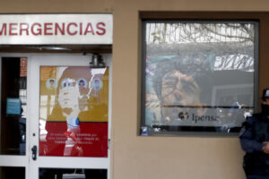 A police officer stands outside the hospital where Diego Maradona is hospitalized and where images of him placed by fans are reflected in the windows, in La Plata, Argentina Tuesday, Nov. 3, 2020. Maradona was admitted to the hospital with signs of depression Monday, three days after his 60th birthday. (AP Photo/ Natacha Pisarenko)