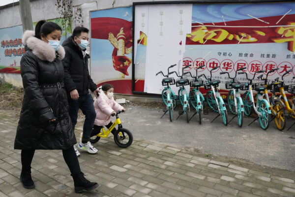 Residents past by government propaganda along a wall near the Service Center for Party Members and Residents of Jiangxinyuan Community where the World Health Organization team is making a field visit in Wuhan in central China’s Hubei province on Thursday, Feb. 4, 2021. (AP Photo/Ng Han Guan)