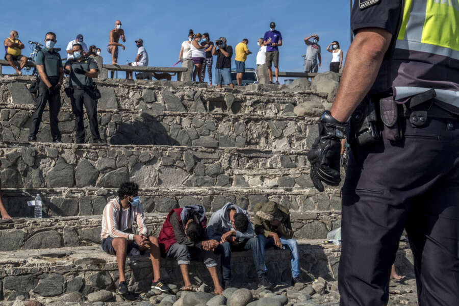 Migrants, most of them from Morocco, are watched by Spanish Police after arriving at the coast of the Canary Islands, Spain on Monday, Nov. 23, 2020, after crossing the Atlantic Ocean sailing on a wooden boat. (AP Photo/Javier Bauluz)