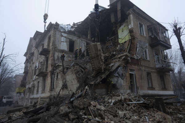 Ukrainian State Emergency Service firefighters clear the rubble at the building which was destroyed by a Russian attack in Kryvyi Rih, Ukraine, Friday, Dec. 16, 2022. Russian forces launched at least 60 missiles across Ukraine on Friday, officials said, reporting explosions in at least four cities, including Kyiv. At least two people were killed by a strike on a residential building in central Ukraine, where a hunt was on for survivors. (AP Photo/Evgeniy Maloletka)