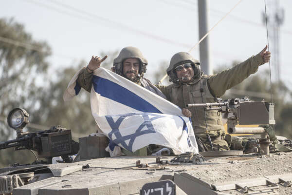 Soldiers wave as they hold an Israeli flag on top on a tank that drives near the border with Lebanon, in Israel, Saturday, Oct. 14, 2023. (AP Photo/Petros Giannakouris)